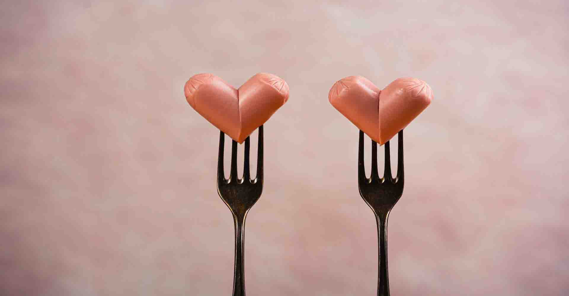 Two funny sausages forming a hearts on a forks on pink background. Wedding or St Valentines day concept. Horizontal, copy space