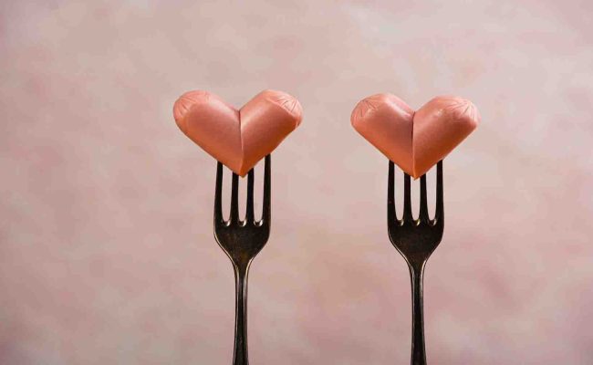 Two funny sausages forming a hearts on a forks on pink background. Wedding or St Valentines day concept. Horizontal, copy space